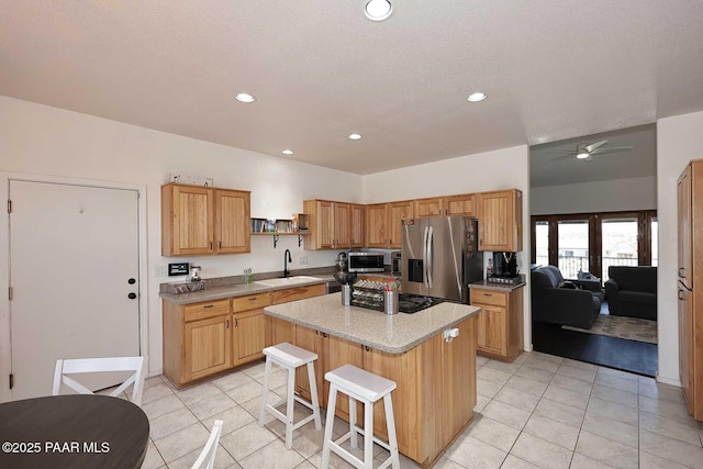 kitchen featuring a kitchen island, ceiling fan, a breakfast bar, appliances with stainless steel finishes, and a sink