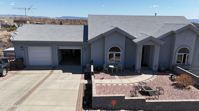 single story home with an attached garage, roof with shingles, stucco siding, driveway, and a mountain view