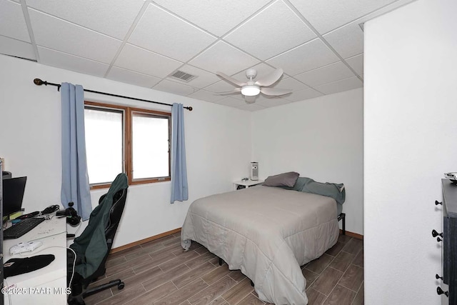 bedroom with baseboards, visible vents, a drop ceiling, and wood finish floors