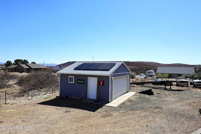 view of outbuilding featuring solar panels, dirt driveway, fence, an outbuilding, and a mountain view