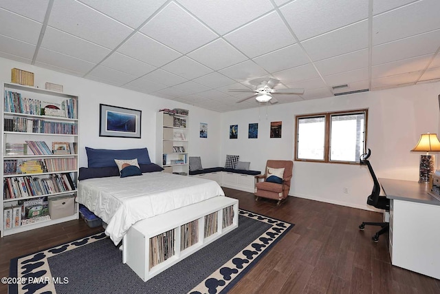 bedroom featuring visible vents, a ceiling fan, a drop ceiling, wood finished floors, and baseboards