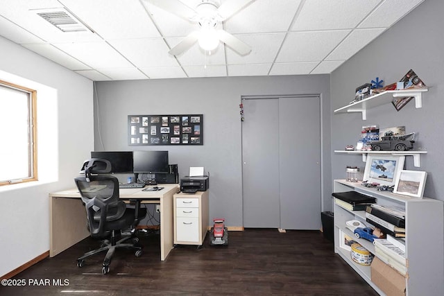 home office featuring baseboards, visible vents, dark wood finished floors, ceiling fan, and a paneled ceiling