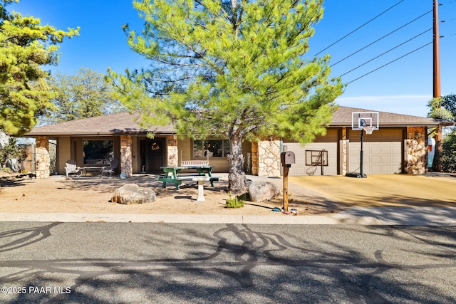 view of front facade with a garage, stone siding, roof with shingles, and concrete driveway