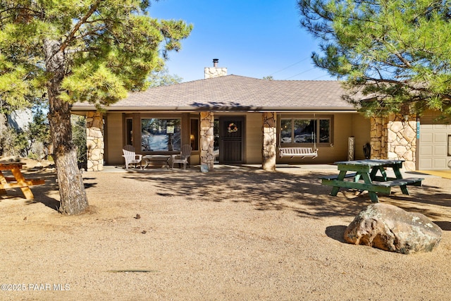 single story home with a shingled roof, stone siding, and a chimney