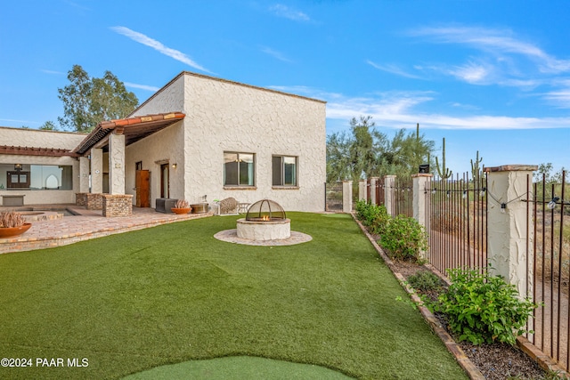 back of property with a lawn, a patio, and an outdoor fire pit