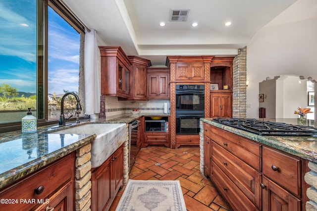 kitchen featuring gas cooktop, tasteful backsplash, dark stone counters, double oven, and sink