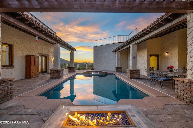 pool at dusk featuring a fire pit, a patio area, and an in ground hot tub