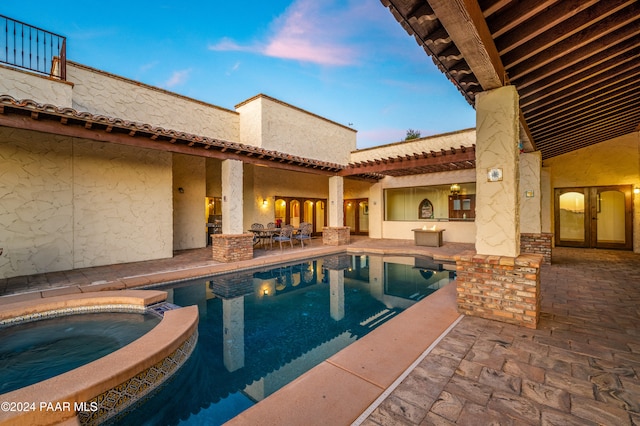 pool at dusk featuring a patio area and an in ground hot tub