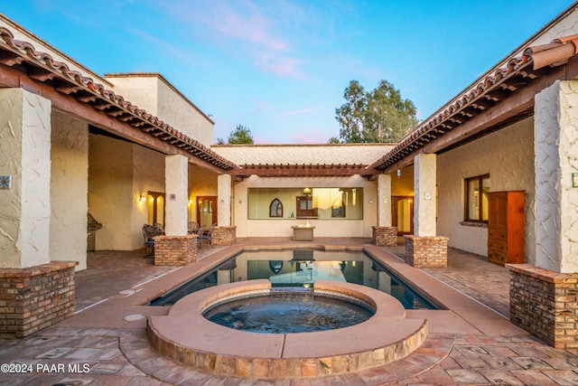 pool at dusk with an in ground hot tub and a patio