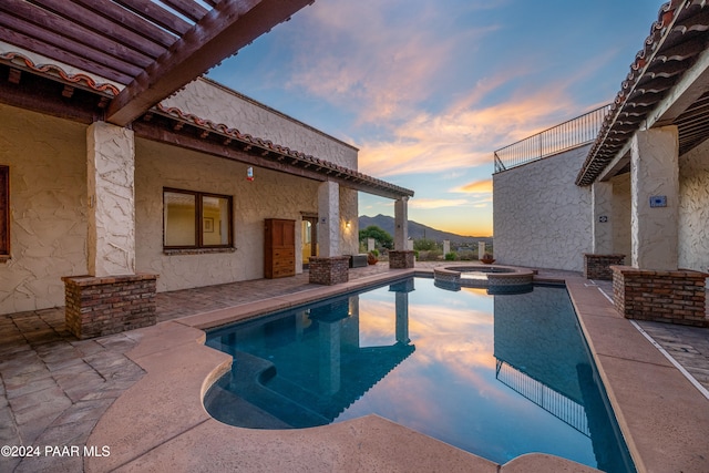 pool at dusk featuring a mountain view, an in ground hot tub, and a patio