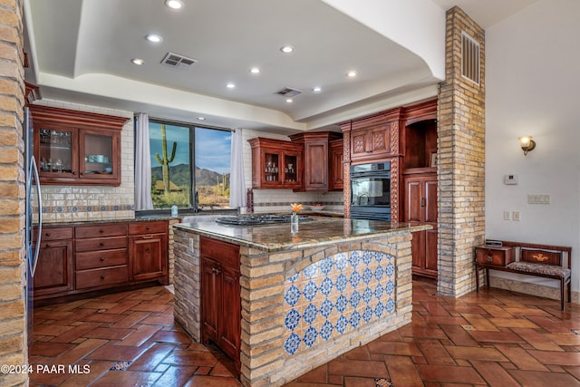 kitchen with decorative backsplash, dark stone countertops, an island with sink, and stainless steel gas cooktop