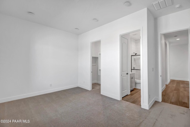 unfurnished bedroom with baseboards, a walk in closet, visible vents, and light colored carpet