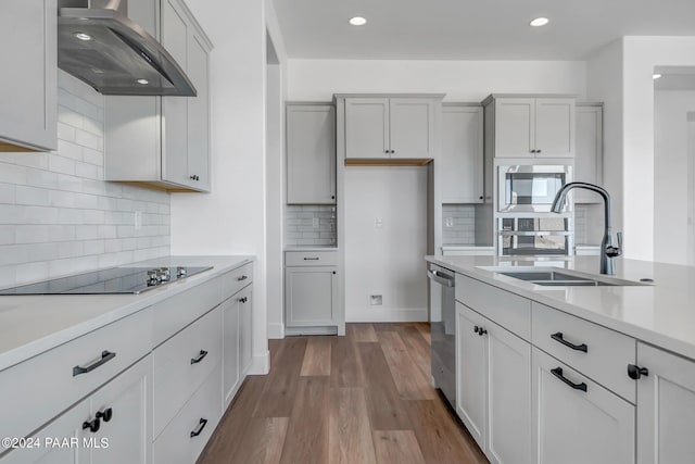 kitchen featuring stainless steel appliances, a sink, light countertops, wall chimney range hood, and light wood finished floors