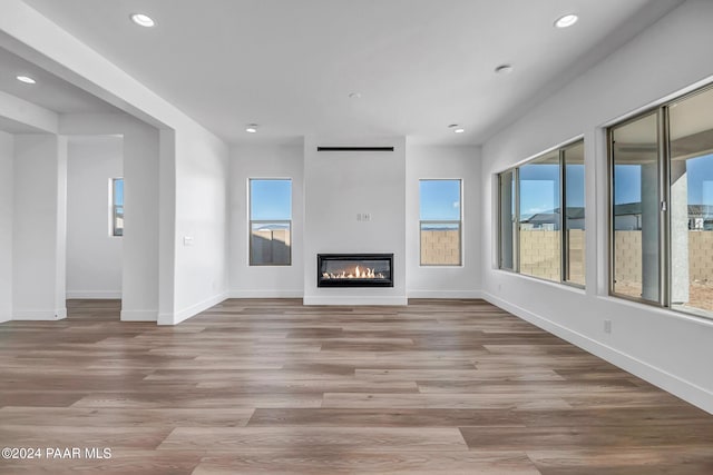 unfurnished living room featuring light wood-style floors, a glass covered fireplace, a wealth of natural light, and recessed lighting