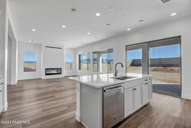 kitchen featuring sink, white cabinets, stainless steel dishwasher, a center island with sink, and light wood-type flooring