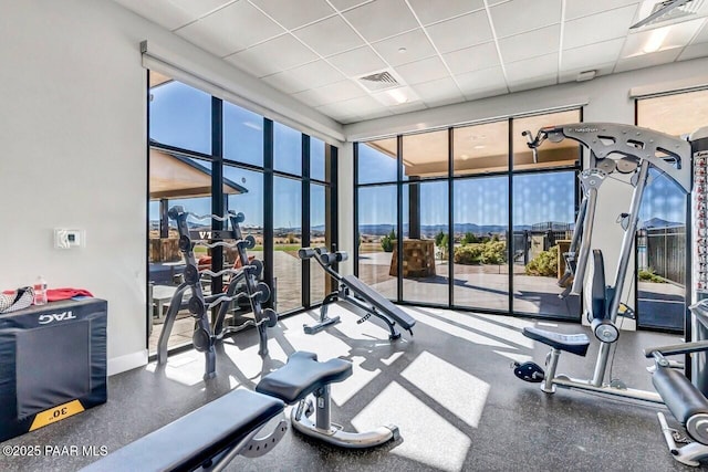 exercise room featuring a paneled ceiling, visible vents, and baseboards