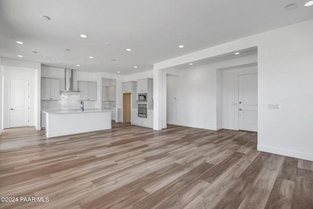 unfurnished living room featuring baseboards, light wood-type flooring, a sink, and recessed lighting