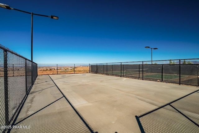 view of basketball court with a tennis court and fence