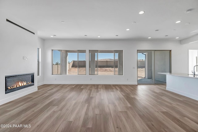 unfurnished living room featuring light wood-style floors, recessed lighting, baseboards, and a glass covered fireplace