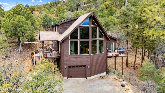 view of home's exterior with stairs, an attached garage, a deck, driveway, and a wooded view