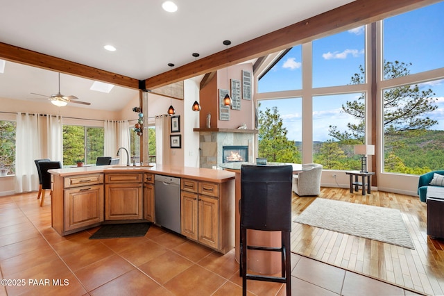 kitchen featuring stainless steel dishwasher, light countertops, lofted ceiling with skylight, open floor plan, and light tile patterned flooring