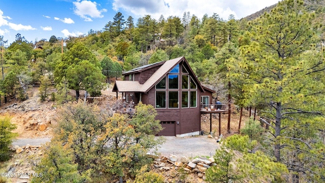 back of property featuring a wooden deck, dirt driveway, an attached garage, and a forest view
