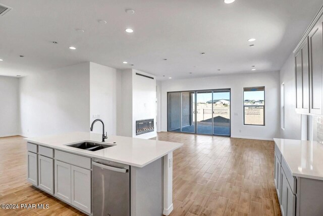 kitchen featuring gray cabinetry, a kitchen island with sink, sink, light hardwood / wood-style flooring, and stainless steel dishwasher