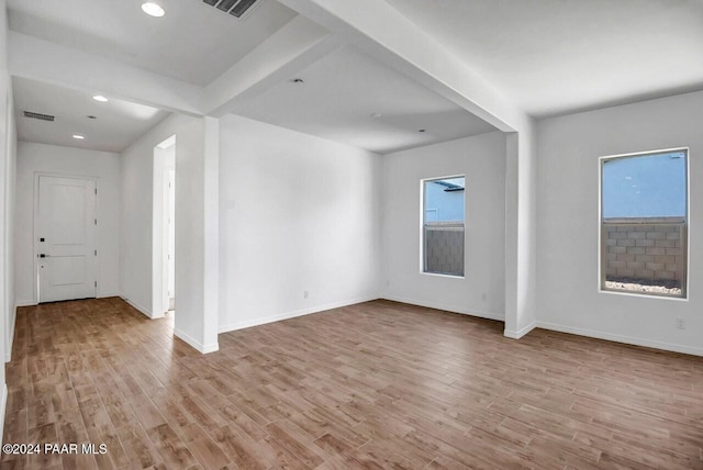 unfurnished room with beam ceiling, light wood-type flooring, and a healthy amount of sunlight