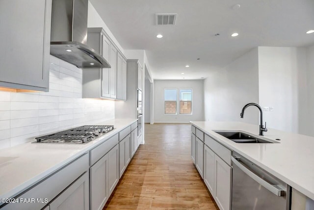 kitchen with gray cabinetry, wall chimney exhaust hood, stainless steel appliances, sink, and light hardwood / wood-style flooring