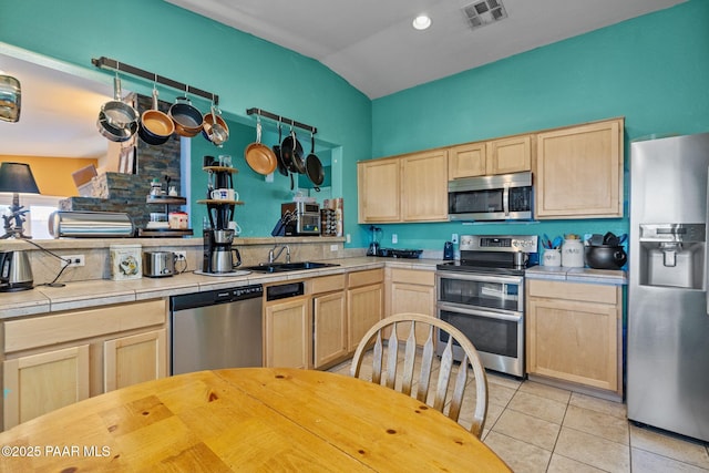 kitchen with lofted ceiling, sink, light brown cabinets, appliances with stainless steel finishes, and tile counters