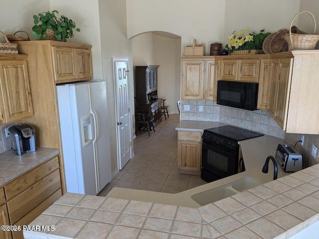 kitchen with backsplash, light tile patterned flooring, tile countertops, and black appliances