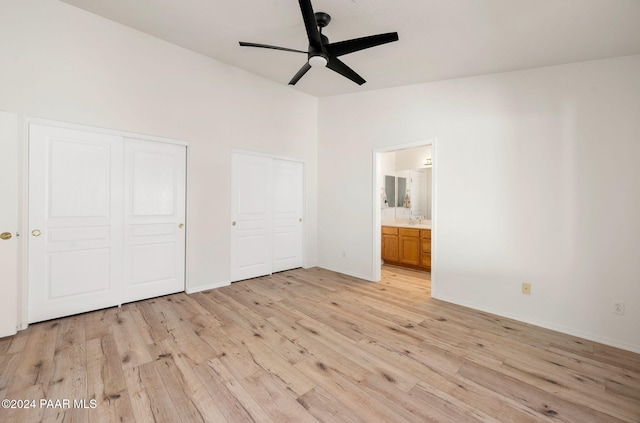 unfurnished bedroom featuring connected bathroom, ceiling fan, light hardwood / wood-style floors, and two closets