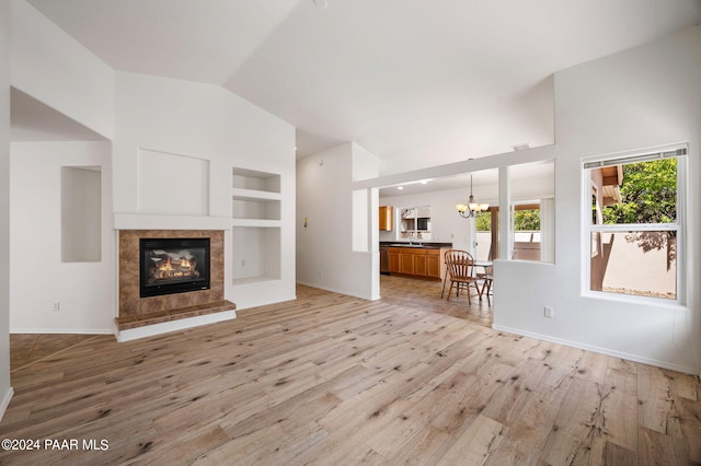 unfurnished living room with a tile fireplace, an inviting chandelier, vaulted ceiling, built in shelves, and light wood-type flooring