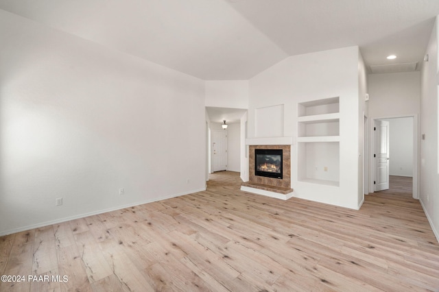 unfurnished living room featuring built in shelves, vaulted ceiling, and light hardwood / wood-style flooring