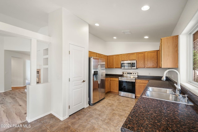 kitchen featuring appliances with stainless steel finishes, light hardwood / wood-style floors, vaulted ceiling, and sink