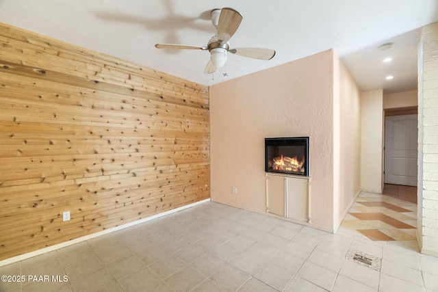 unfurnished living room featuring ceiling fan, wooden walls, and light tile patterned floors