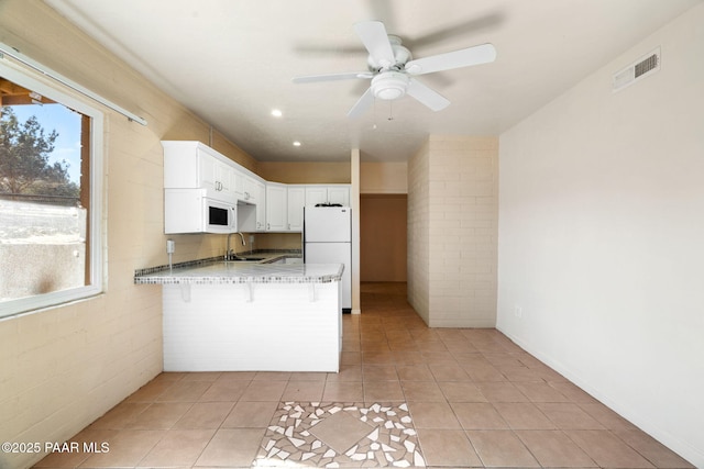 kitchen with white appliances, a kitchen breakfast bar, light stone countertops, white cabinets, and kitchen peninsula