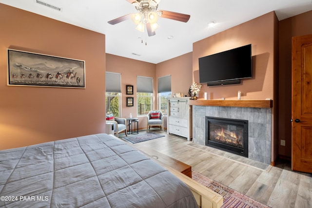 bedroom featuring hardwood / wood-style floors, ceiling fan, and a tiled fireplace