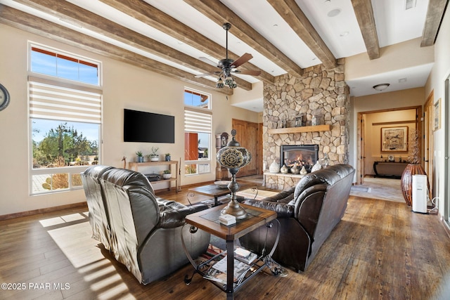 living room featuring a stone fireplace, beamed ceiling, hardwood / wood-style floors, and baseboards