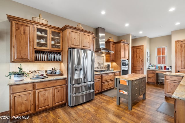 kitchen with decorative backsplash, appliances with stainless steel finishes, light stone counters, wall chimney exhaust hood, and dark wood-type flooring