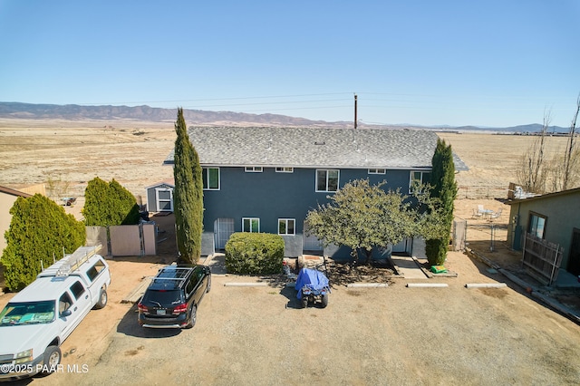 back of property featuring uncovered parking, stucco siding, a mountain view, and fence