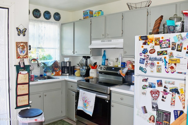 kitchen with under cabinet range hood, a sink, stainless steel range with electric cooktop, freestanding refrigerator, and light countertops