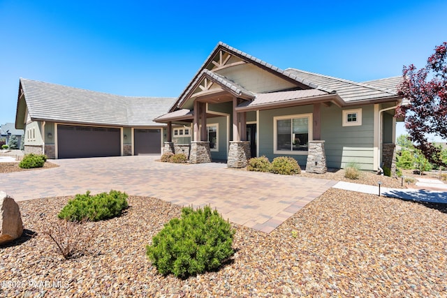 craftsman inspired home with a garage, decorative driveway, and stone siding
