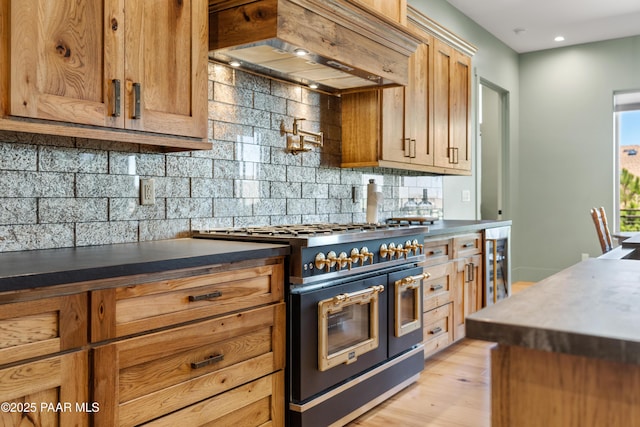 kitchen with decorative backsplash, range with two ovens, beverage cooler, custom range hood, and light wood-style flooring