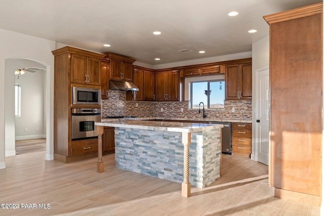 kitchen featuring sink, light stone counters, light hardwood / wood-style floors, a kitchen island, and appliances with stainless steel finishes