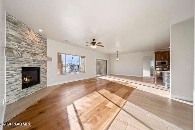 unfurnished living room with a stone fireplace, ceiling fan, and light wood-type flooring