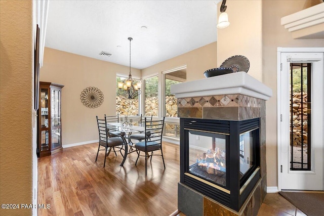 dining space featuring a wealth of natural light, a fireplace, wood-type flooring, and an inviting chandelier