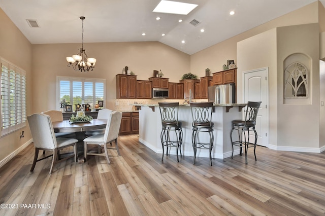 kitchen featuring stainless steel appliances, light hardwood / wood-style flooring, a chandelier, a breakfast bar area, and an island with sink