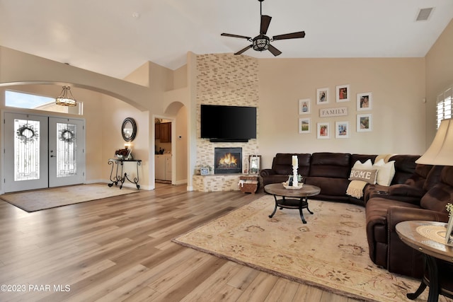 living room featuring ceiling fan, a large fireplace, french doors, high vaulted ceiling, and light hardwood / wood-style floors