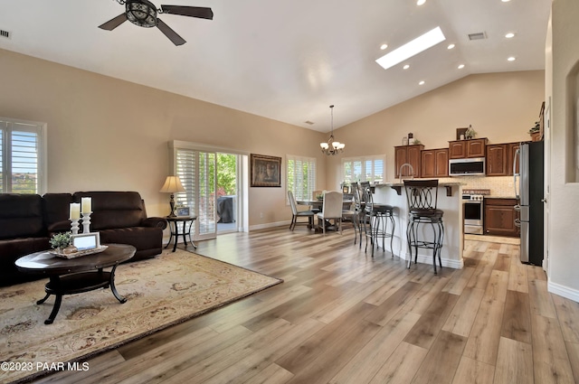 living room featuring a skylight, light hardwood / wood-style flooring, a healthy amount of sunlight, and ceiling fan with notable chandelier